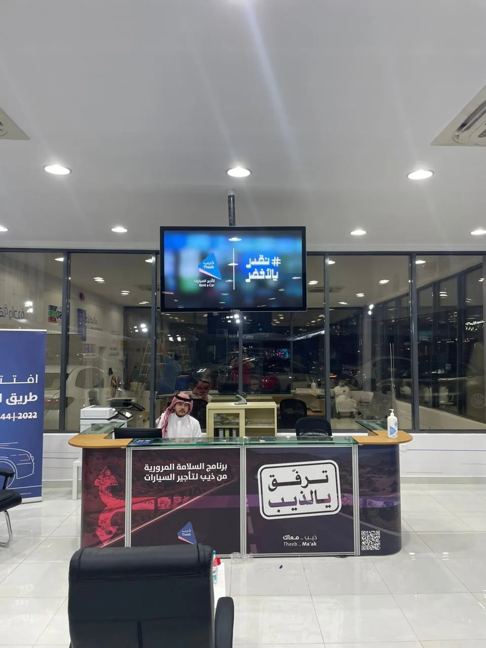 Wall-mounted digital signage screen above a Theeb branch reception desk